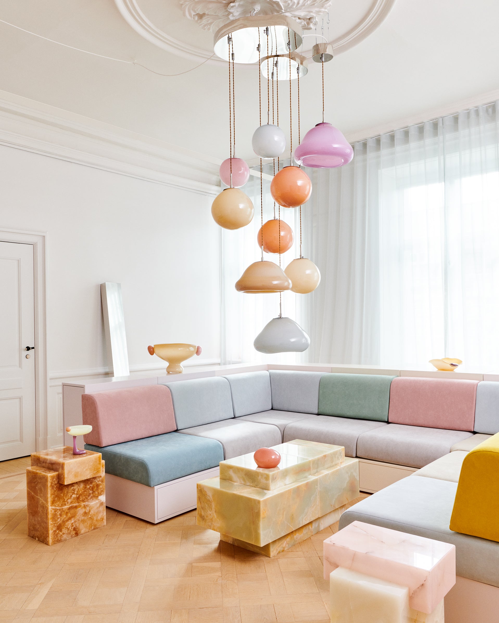 Living room with a sofa, table and glass objects. Lamps hanging in the ceiling in blue, beige, brown, violet and red colors.